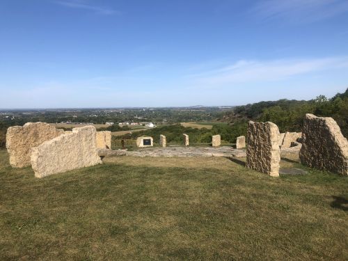 Ancient stone structures on a grassy hill, overlooking a scenic landscape with distant fields and blue sky.