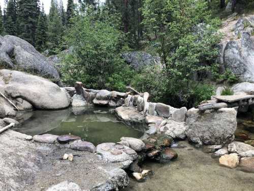 A natural hot spring surrounded by rocks and trees, with a small wooden bridge nearby.