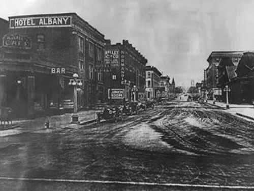 Historic black-and-white photo of a street scene featuring Hotel Albany and various storefronts.