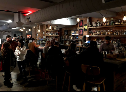 A lively bar scene with patrons socializing, a long bar stocked with bottles, and warm lighting creating a cozy atmosphere.