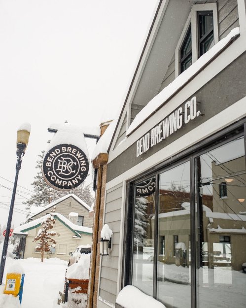 Exterior of Bend Brewing Company, featuring a snowy scene and a sign with the brewery's logo.