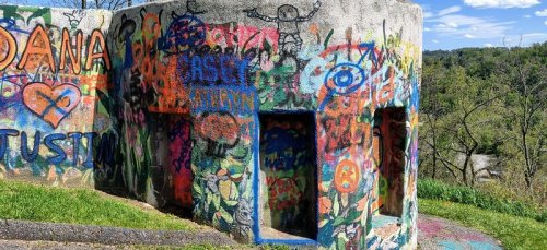 A colorful, graffiti-covered concrete structure surrounded by greenery and blue skies.