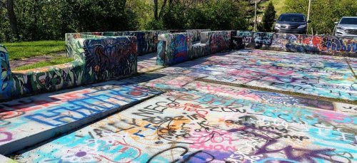 A concrete area covered in colorful graffiti, surrounded by greenery and parked cars in the background.