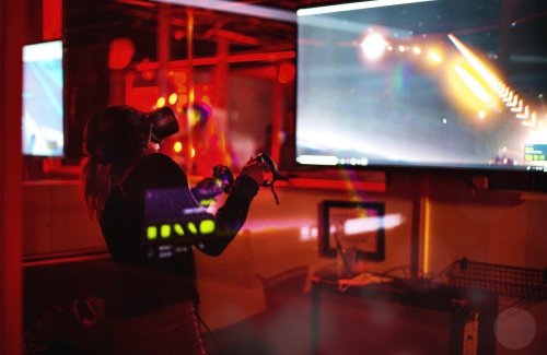 A person wearing a VR headset interacts with a virtual environment, illuminated by red lighting and a large screen.