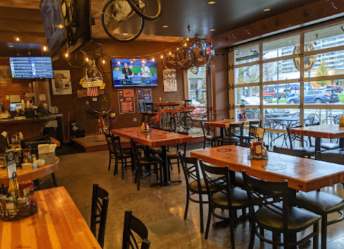 Interior of a casual restaurant with wooden tables, chairs, and TVs showing sports, featuring a bike-themed decor.