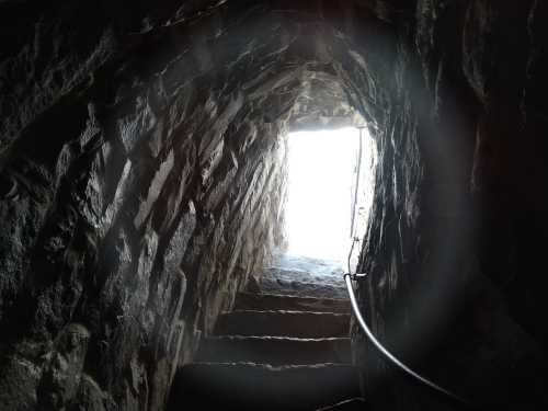 A dimly lit stone staircase leading up to a bright opening at the top, framed by rough rock walls.