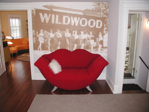 A red lip-shaped sofa in a room with a vintage Wildwood mural and a cozy atmosphere.