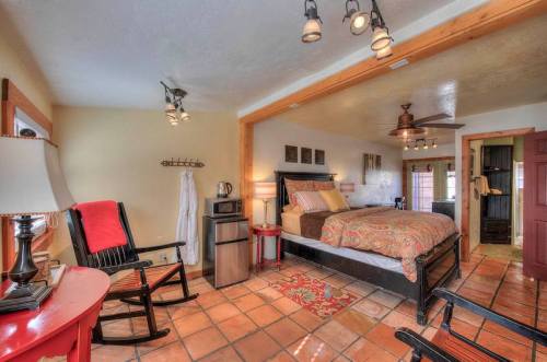 Cozy bedroom with a queen bed, rocking chairs, mini fridge, and warm lighting, featuring tiled floors and rustic decor.