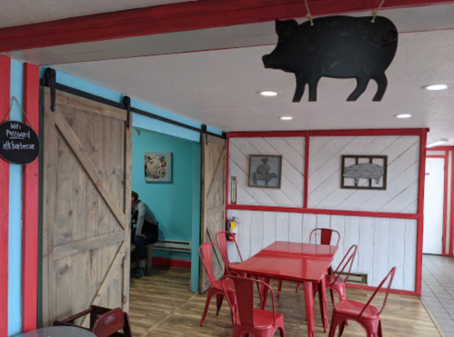 Interior of a casual dining space with red tables, wooden doors, and a pig decoration hanging from the ceiling.