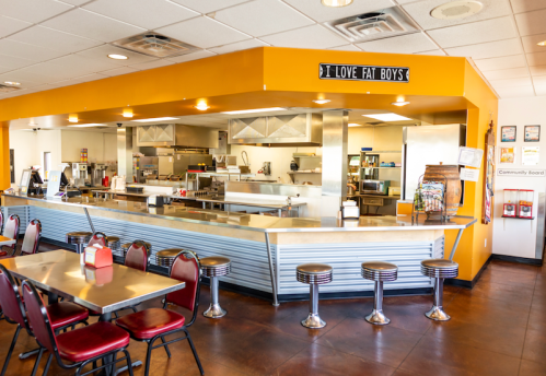 A bright diner interior with a counter, stools, and a sign that reads "I Love Fat Boys."