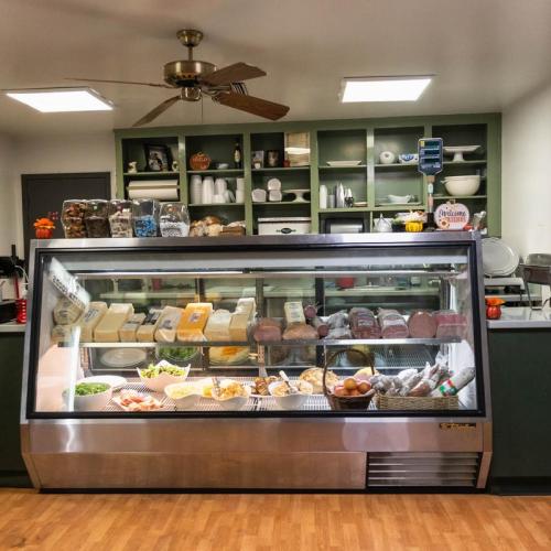 A display case filled with various meats, cheeses, and fresh produce in a cozy, well-lit deli setting.