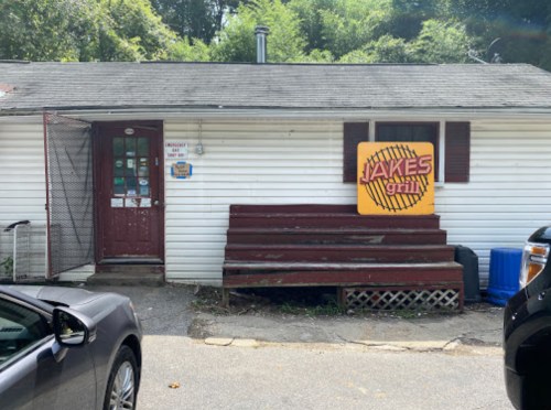 A small white building with a red door and a large sign reading "Jake's Grill" above wooden steps.