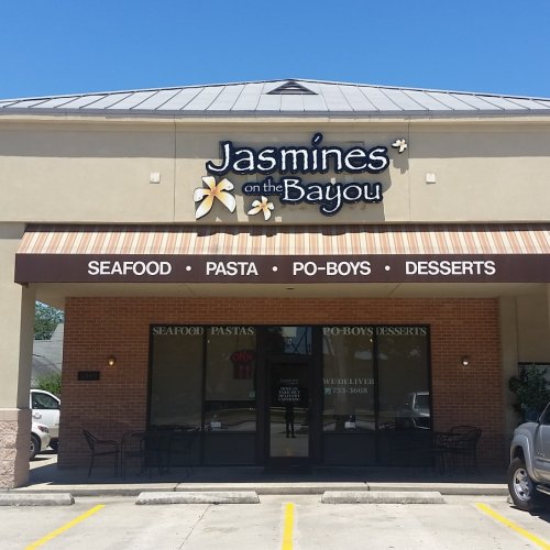 Sign for "Jasmines on the Bayou" restaurant featuring seafood, pasta, po-boys, and desserts. Outdoor seating visible.