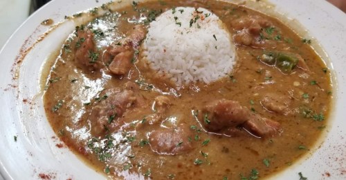 A plate of savory stew with tender meat and herbs, served with a mound of white rice on top.