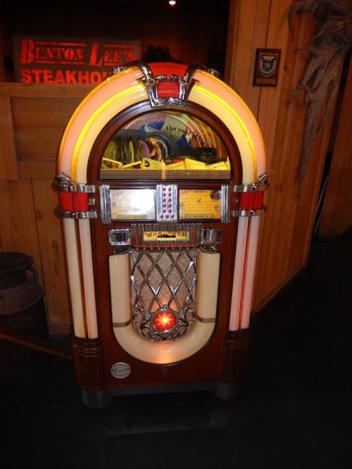 A vintage jukebox with a classic design, featuring bright lights and a shiny chrome finish, set in a rustic environment.