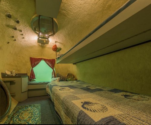 Cozy, uniquely designed interior of a small room with a bed, shelves, and a window, featuring soft green lighting.
