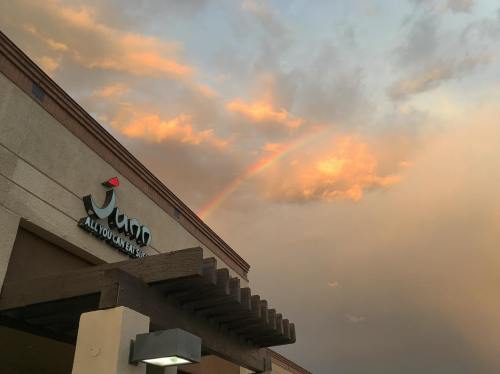 A building with a sign reading "Juno" under a colorful sunset and a rainbow in the sky.
