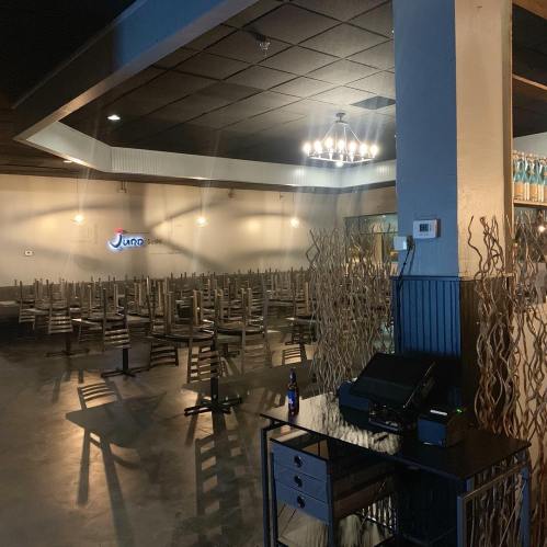 Empty restaurant interior with stacked chairs, a dark ceiling, and a small bar area. Soft lighting and decor visible.