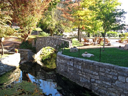 A serene scene featuring a stone bridge over a calm stream, surrounded by colorful trees and a picnic area.