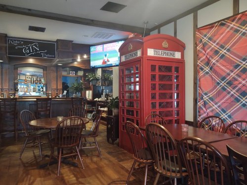 A cozy restaurant interior featuring a red telephone booth, wooden tables, and a bar with a TV in the background.