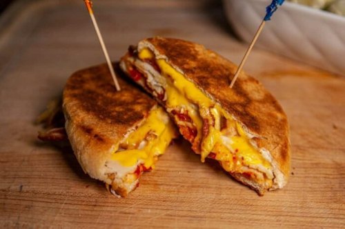 A toasted sandwich filled with melted cheese, chicken, and bacon, secured with toothpicks, on a wooden cutting board.