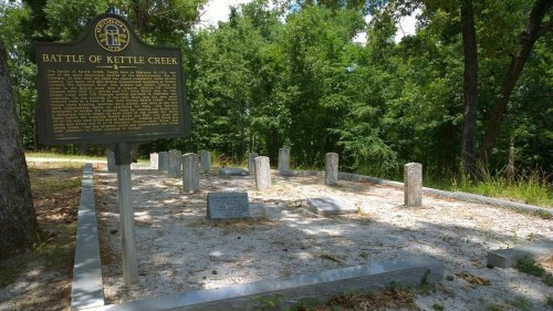 Historical marker at the Battle of Kettle Creek site, surrounded by gravestones and trees in a serene setting.