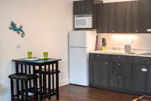 A modern kitchen with dark cabinets, a white fridge, a microwave, and a small dining table with green glasses.