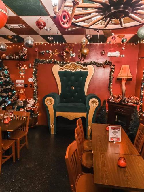 A festive restaurant interior featuring a large green throne, decorated with Christmas lights and ornaments.