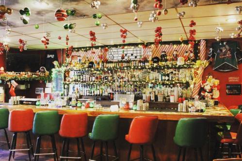 A festive bar decorated with holiday ornaments, lights, and a variety of bottles on the shelves.