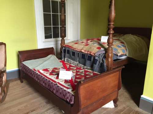 Two wooden beds with colorful quilts in a room with yellow walls and a door in the background.