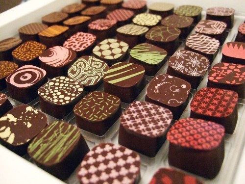 A variety of beautifully decorated chocolate squares arranged in a box, showcasing intricate patterns and colors.
