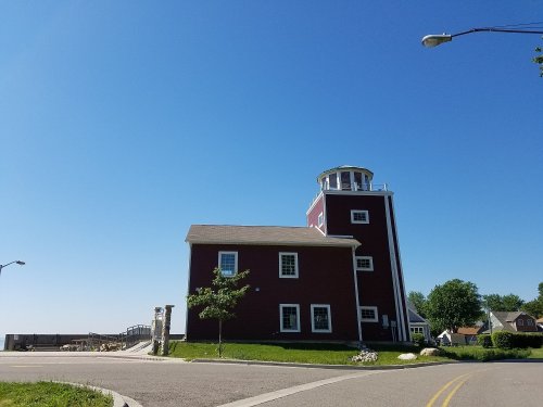 A red barn-style building with a tower, set against a clear blue sky and green grass, near a road.