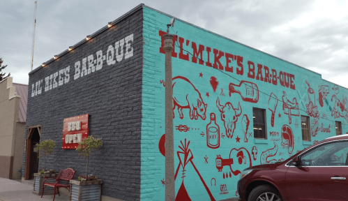 Exterior of a barbecue restaurant with colorful murals and a sign reading "All Mike's Bar-B-Que" and "BBQ Open."