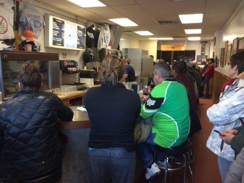 A busy diner interior with customers seated at the counter, waiting for food, and staff preparing meals in the background.