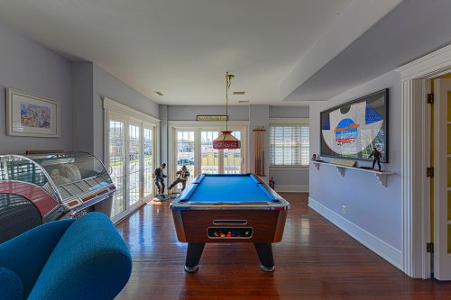 A bright room featuring a blue pool table, jukebox, and large windows with views outside.