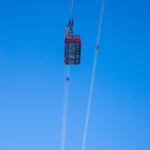 A cable car suspended in the sky, with clear blue background and cables extending from it.
