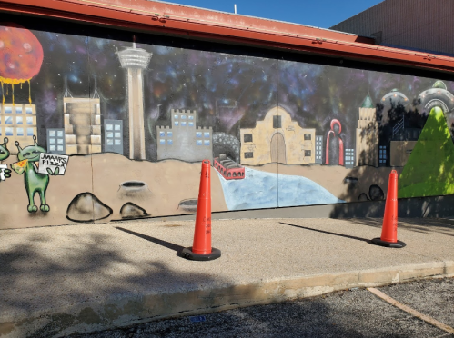 Colorful mural featuring a cityscape, aliens, and UFOs, with traffic cones in the foreground.