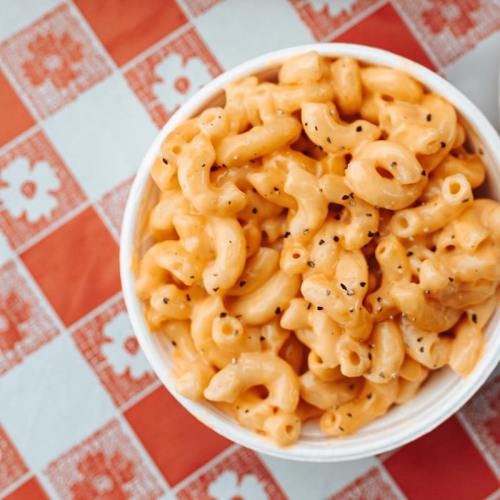 A bowl of creamy macaroni and cheese topped with black pepper, set on a red and white checkered tablecloth.