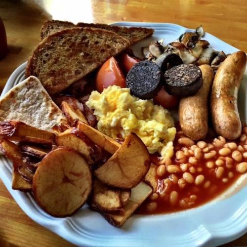 A hearty breakfast plate with toast, scrambled eggs, baked beans, sausage, black pudding, tomatoes, and fried potatoes.