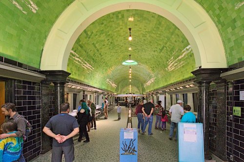 A vibrant, green-tiled underground corridor with people walking and exploring the space.