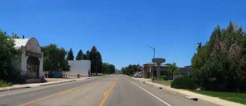 A wide, empty street lined with trees and buildings under a clear blue sky.