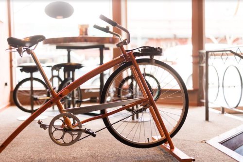 A stylish orange bicycle stands in a cozy café with tables and chairs in the background.