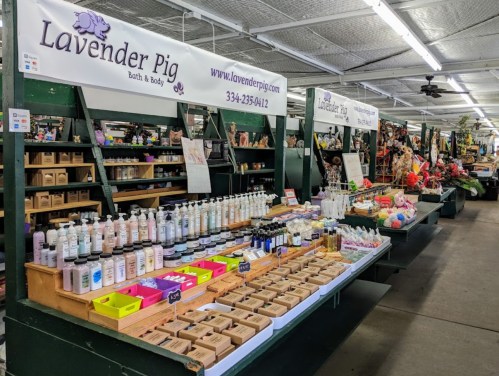 A market stall displaying various lavender-themed bath and body products, with signage for "Lavender Pig."