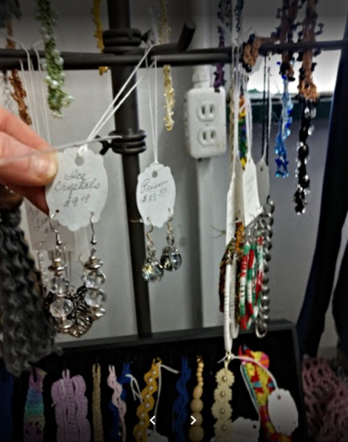 A hand holding a pair of earrings among various jewelry pieces displayed on a rack.