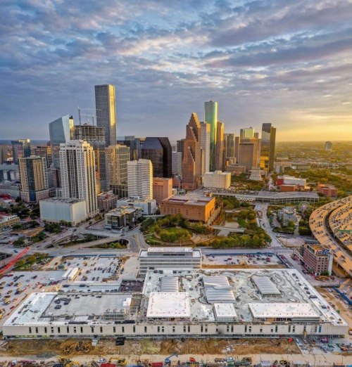 Aerial view of a city skyline at sunset, featuring modern skyscrapers and construction in the foreground.