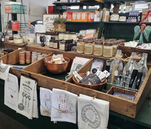 A display of various home goods, including candles, kitchen towels, and decorative items, arranged in wooden trays.