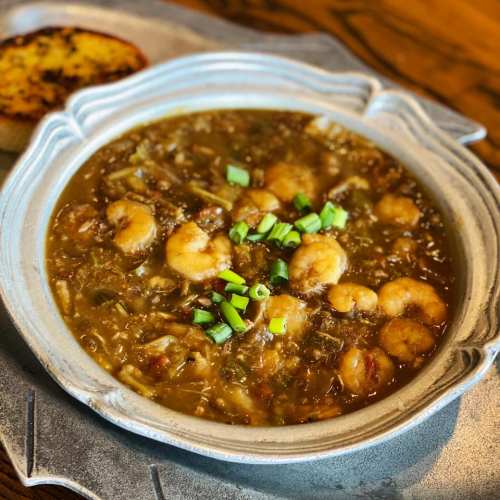 A bowl of shrimp gumbo topped with green onions, served with a piece of toasted bread on the side.