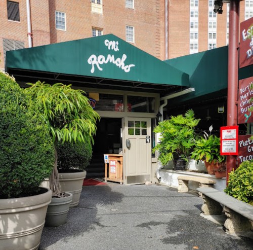 Entrance to Mi Ranchos restaurant, featuring green awnings and potted plants in a brick building setting.