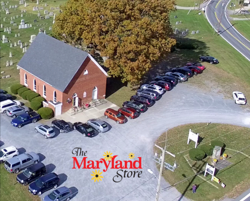 Aerial view of a church with parked cars and a nearby road, featuring "The Maryland Store" logo at the bottom.