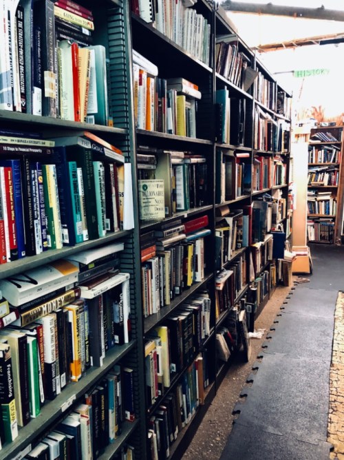 A narrow aisle between tall bookshelves filled with various books in a cozy library setting.